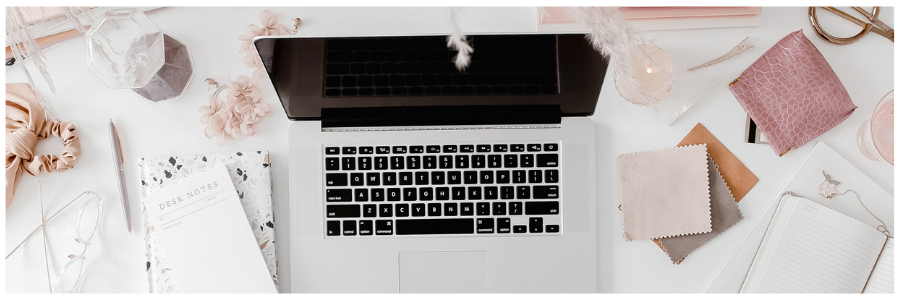 Laptop open on a desk with a lot of office supplies and fabric samples